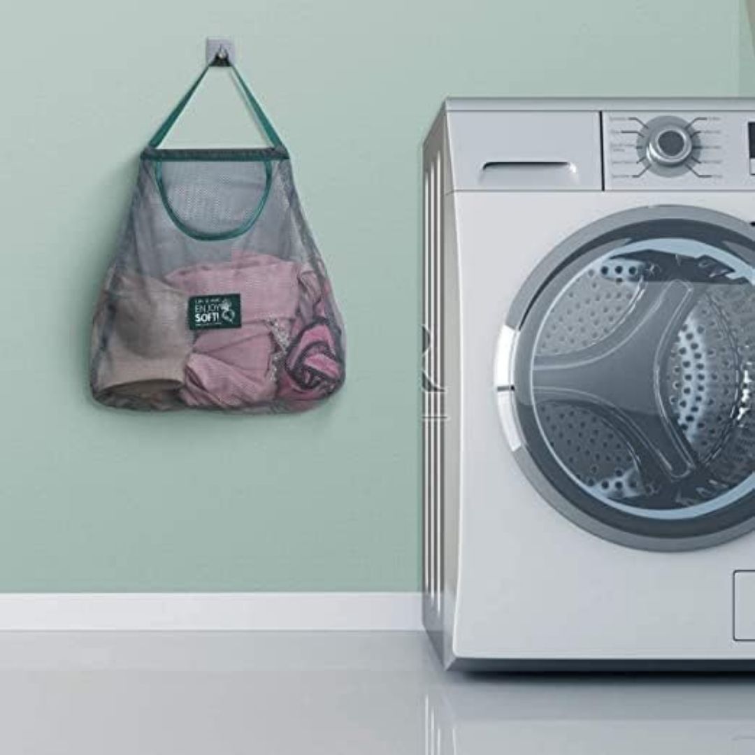 Laundry bag with clothes hanging on a washing machine against a light green wall.