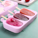 Pink silicone popsicle mold with three frozen popsicles on a green surface