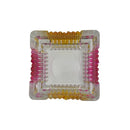 Top view of square glass ashtray with ribbed pink and yellow sides, clear base, and modern aesthetic
